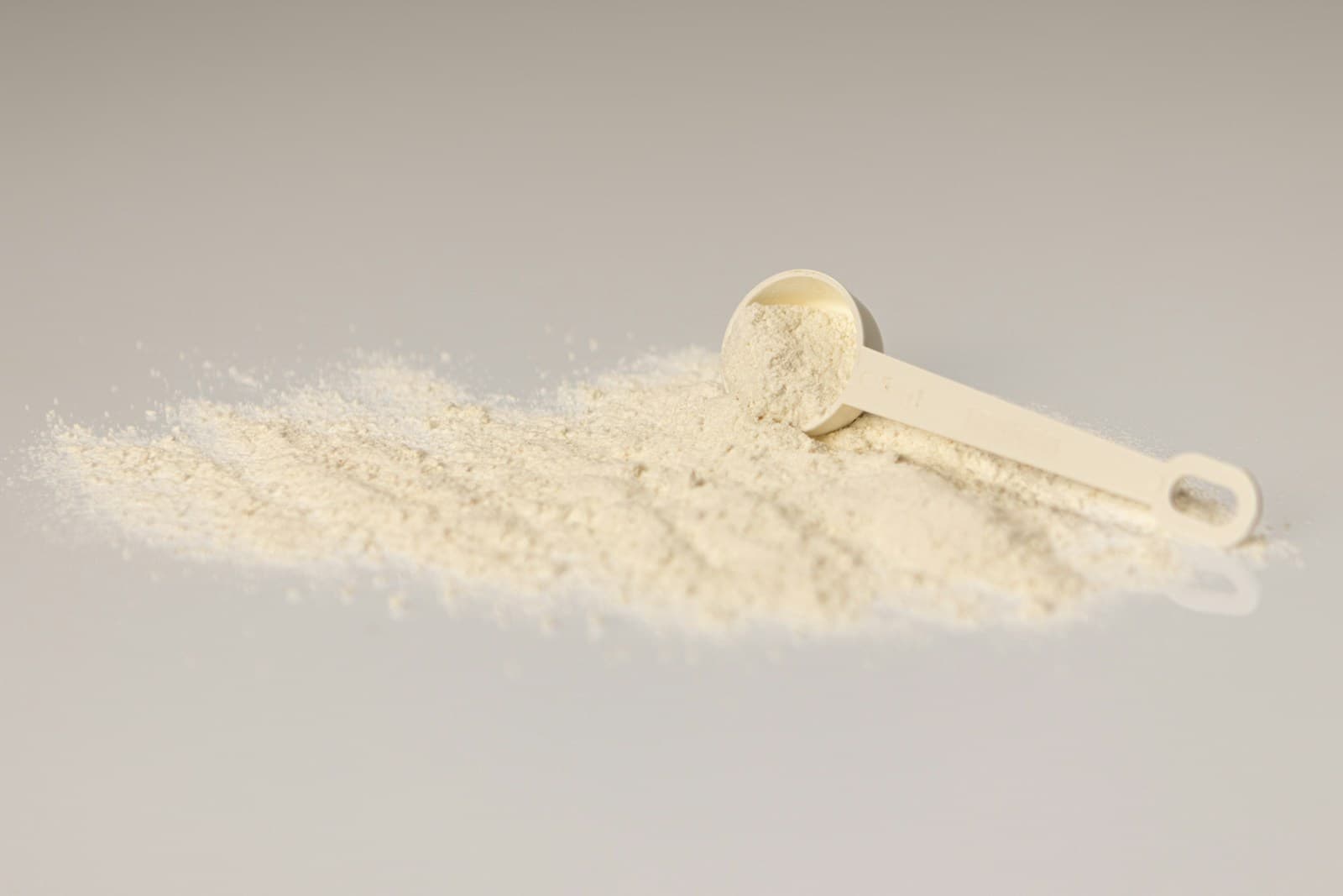 Cosmetic ingredient powder with a measuring scoop on an ivory surface — representative of how Pepoderma ships Matrixyl (Palmitoyl Pentapeptide-4) as a lipidated bulk active for anti-aging serum runs.