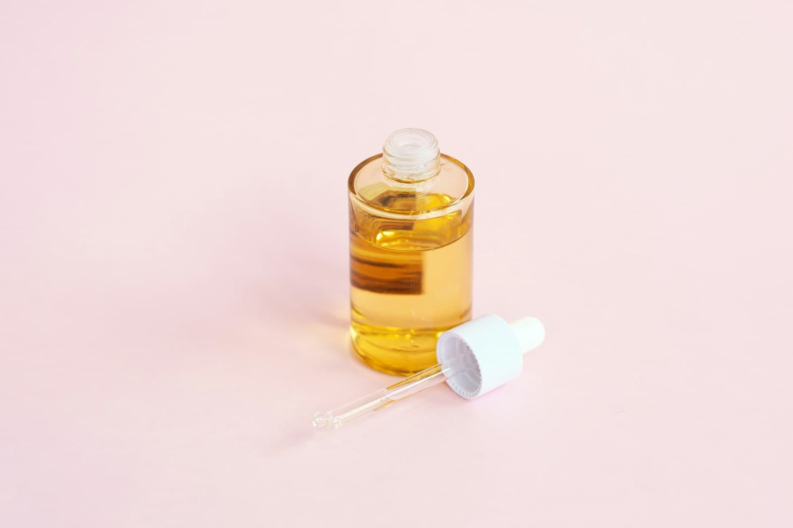 Editorial still life of a cosmetic dropper bottle with amber serum on a soft pink surface — representative of Pepoderma cosmetic-grade peptide actives packaged for indie beauty brand formulation work.