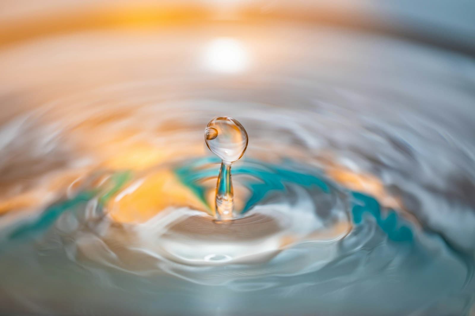 Macro photograph of a water droplet impacting a still water surface, golden-cyan light catching the ripple — editorial visual for the Pepoderma Journal cosmetic-formulation briefings.